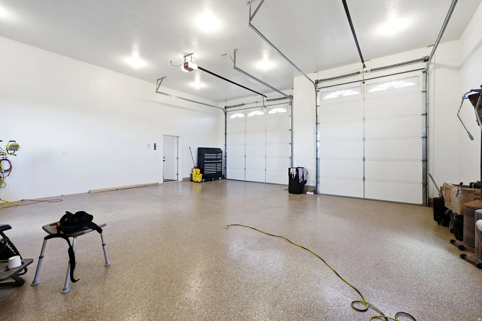 Spacious garage with an epoxy-coated floor, two overhead garage doors with window inserts, and bright overhead lighting