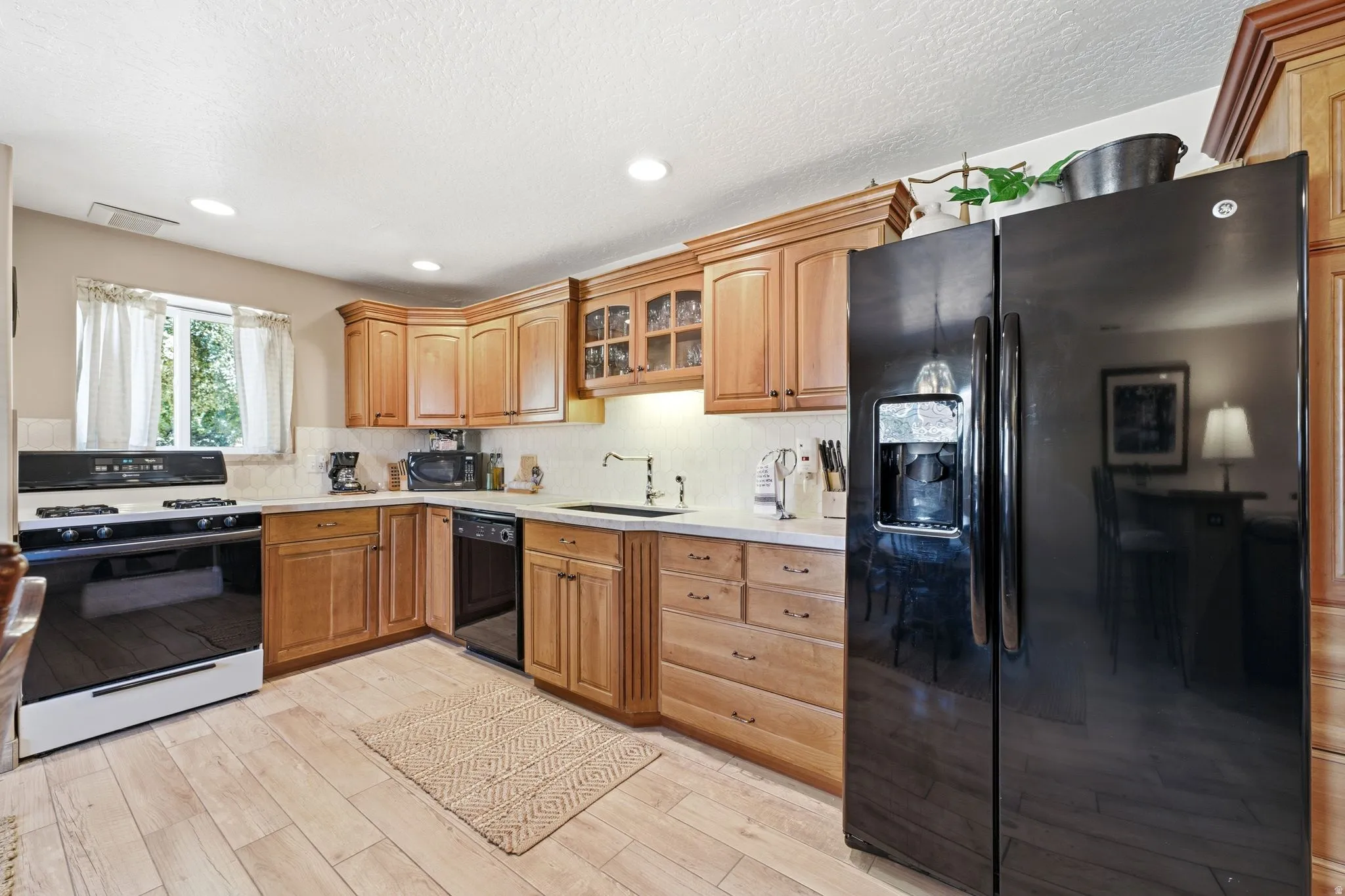 Lower level Kitchen featuring wood-finish flooring, light wood cabinetry, a black side-by-side refrigerator, a black and white range, and a corner sink with a stainless steel faucet