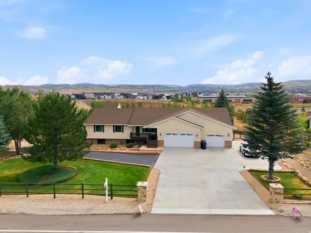 Ranch-style residence featuring a two-car garage, mature trees, and a paved driveway