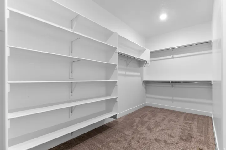 Spacious walk-in closet featuring extensive white shelving, multiple chrome hanging rods, recessed ceiling lighting, and soft brown carpeting