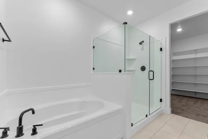 Contemporary bathroom featuring a built-in soaking tub with matte black fixtures, a glass-enclosed shower with matte black hardware, and an adjacent walk-in closet with extensive shelving