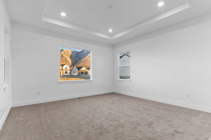 Spacious room featuring neutral carpeting, white walls, and a tray ceiling with recessed lighting
