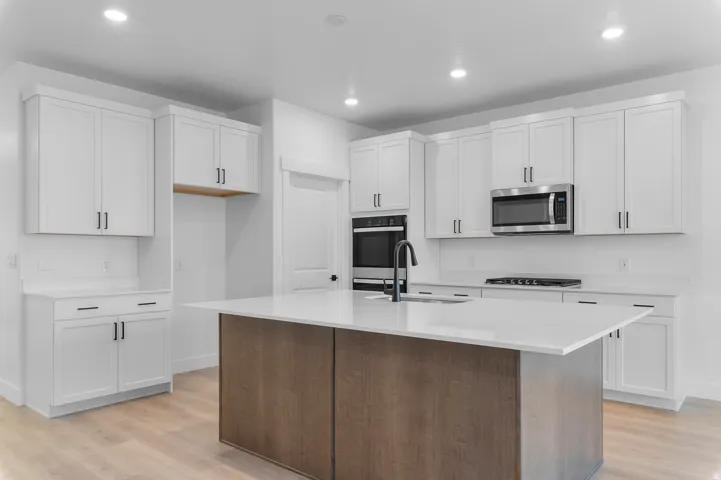 Modern kitchen featuring a two-toned island with a light-toned countertop, white shaker cabinetry, stainless steel appliances, and light wood-finish flooring