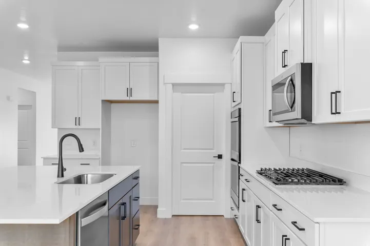 Modern kitchen featuring white cabinetry with black hardware, stainless steel appliances, and light-toned wood-finish flooring