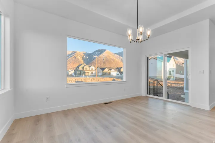 Spacious room featuring a large picture window, a sliding glass door, a contemporary chandelier, light wood-finish flooring, and crisp white walls