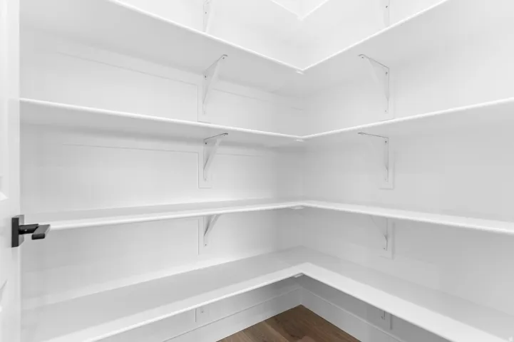Walk-in pantry featuring abundant white shelving, wood-finish flooring, and a contemporary black door handle