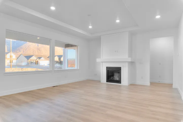 Expansive living space featuring light wood-finish flooring, a contemporary fireplace with a white mantel, and large windows