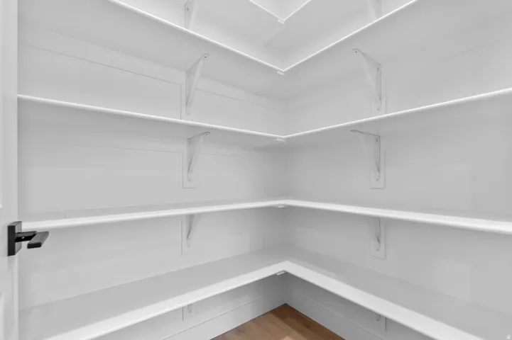 Corner pantry featuring multiple tiers of white shelving, white shiplap-style wall paneling, and wood-finish flooring
