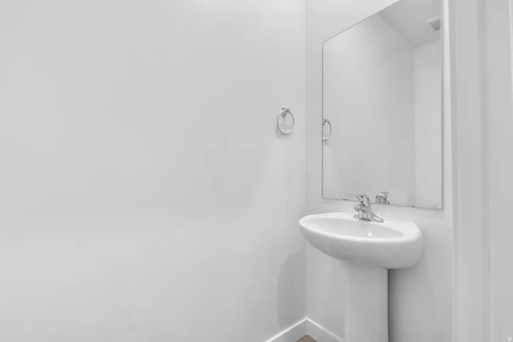 Pedestal sink with chrome faucet, complemented by a wall-mounted mirror and towel ring