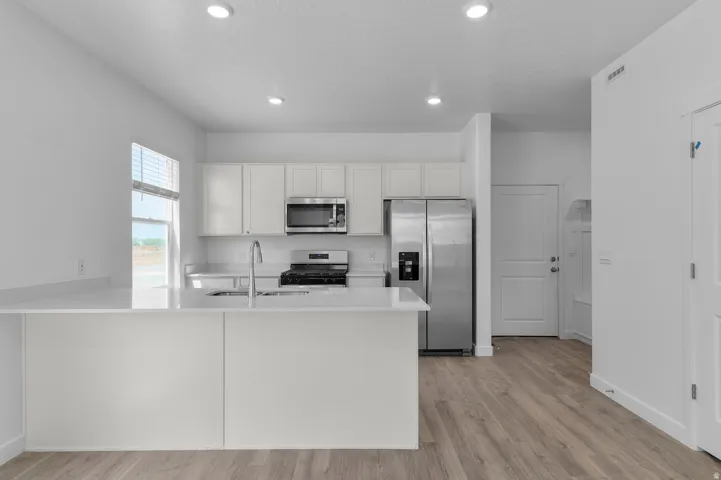 Kitchen featuring white cabinetry, stainless steel appliances, a center island with sink, white countertops, and wood-finish flooring