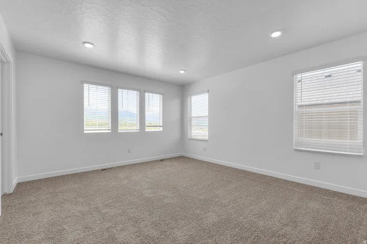 Spacious room featuring neutral carpeting, white walls, multiple windows with blinds, recessed lighting, and white baseboards