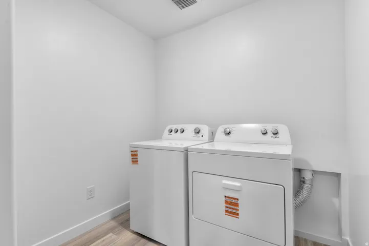 Dedicated utility space featuring a washer and dryer, wood-finish flooring, and white baseboards