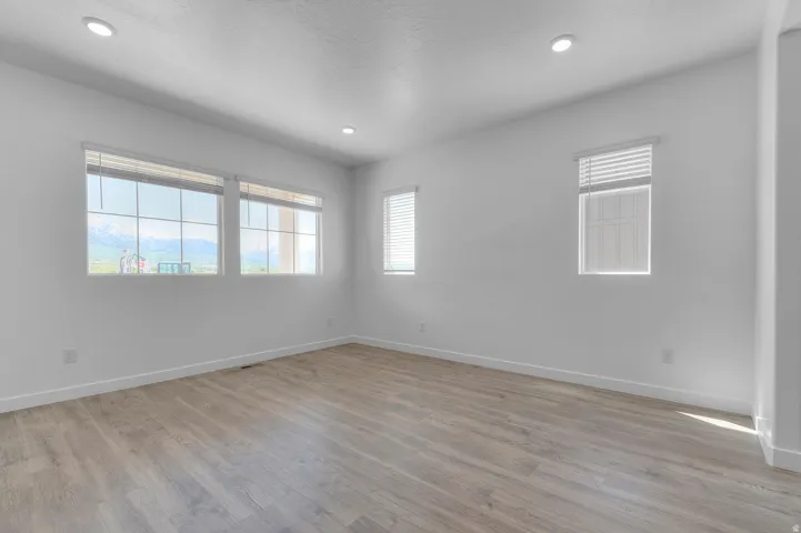 Spacious room featuring multiple windows, wood-finish flooring, recessed lighting, and crisp white walls