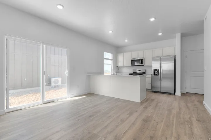 Open-concept living space featuring wood-finish flooring, a contemporary kitchen with white cabinetry, stainless steel appliances, a kitchen island with a white countertop, and recessed lighting