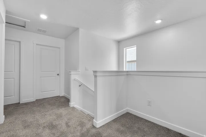 Upper-level landing featuring textured gray carpeting, a white painted railing, and a window with privacy glass