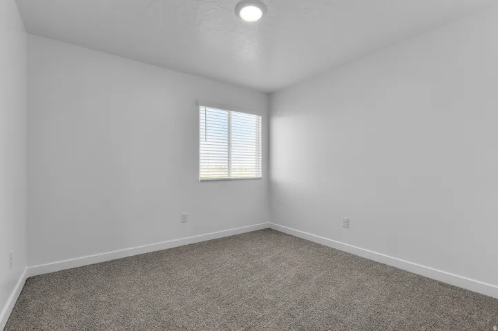 Neutral-toned carpeting paired with white walls, a single window with blinds, and a flush-mount ceiling light fixture