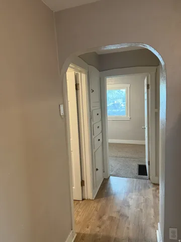 Hallway with light wood-finish flooring and an arched doorway