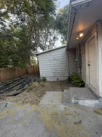 Rear exterior featuring a concrete patio, wood privacy fence, and mature trees