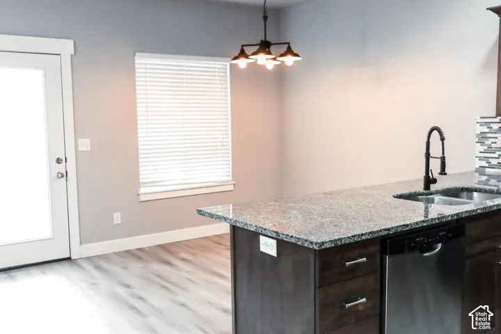 Kitchen island featuring a granite countertop, stainless steel sink with a matte black faucet, and integrated dishwasher
