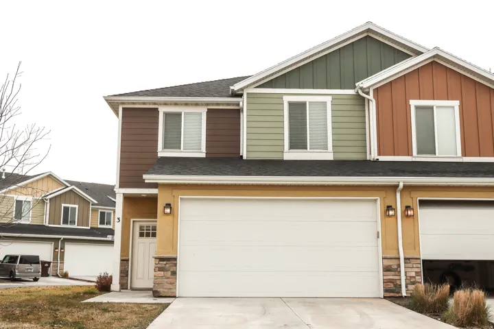 Multi-story townhome featuring a neutral stucco base, horizontal siding in varying earth tones, and a dark shingle roof