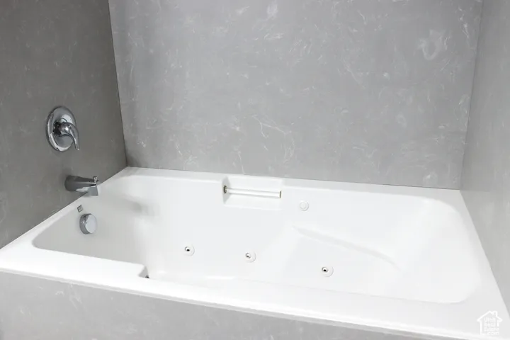 White jetted soaking tub with chrome fixtures and light gray patterned wall surround