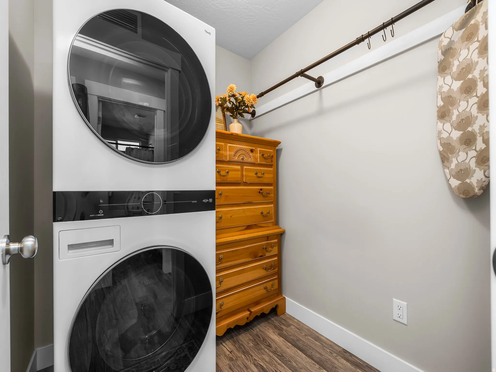 Dedicated laundry area featuring modern stacked appliances, wood-finish flooring, and light gray wall paint
