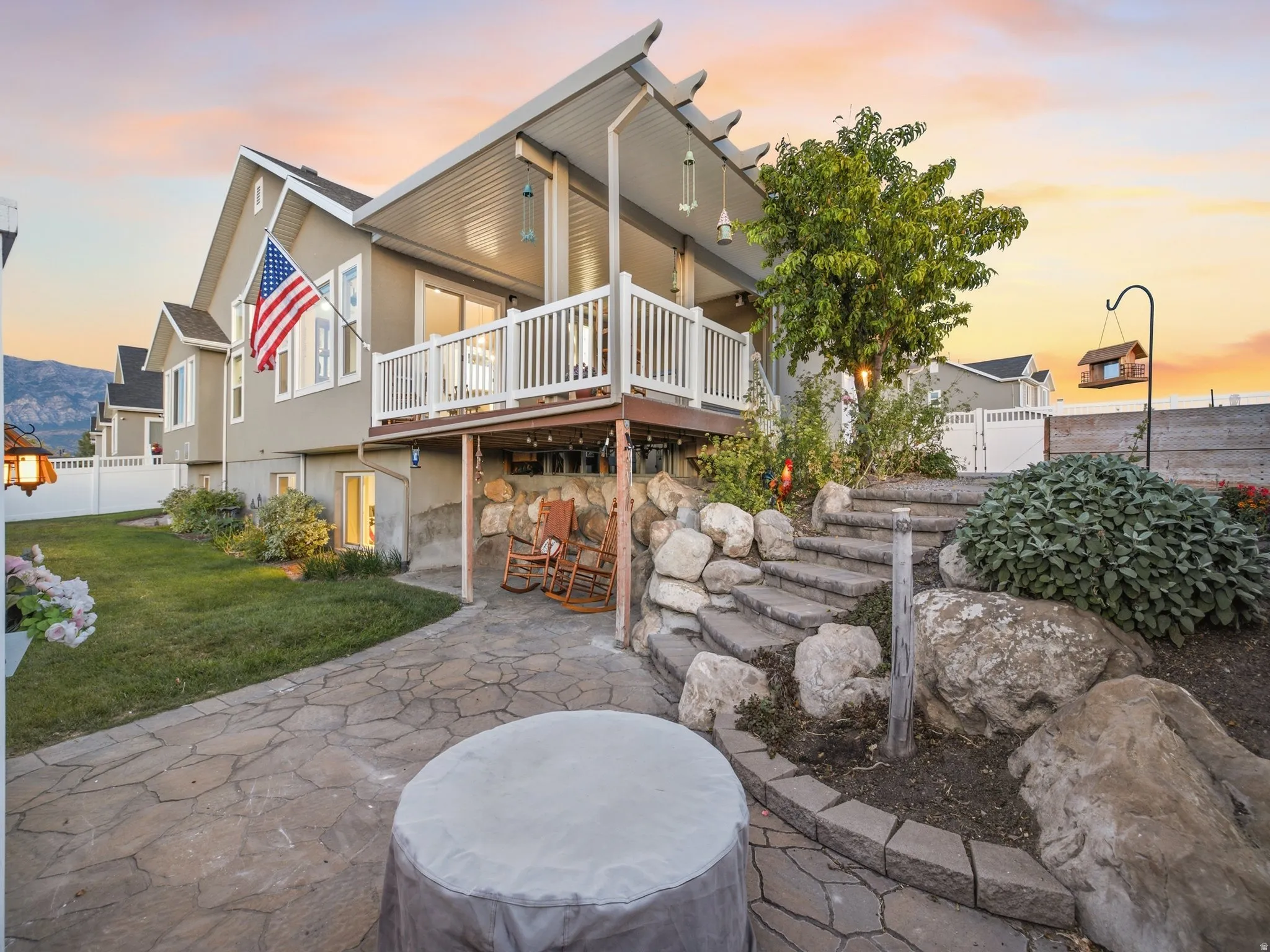 Multi-level outdoor living space featuring an upper deck with white railings, a covered lower patio, and a stone paver patio