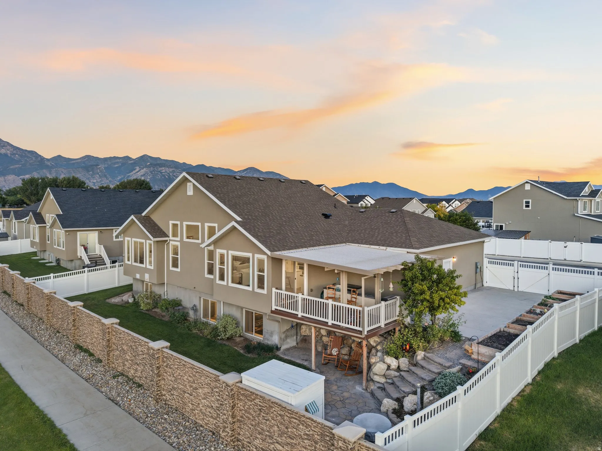 Rear exterior featuring an upper-level covered balcony, lower-level patio with stone steps, a manicured lawn, and mountain scenery
