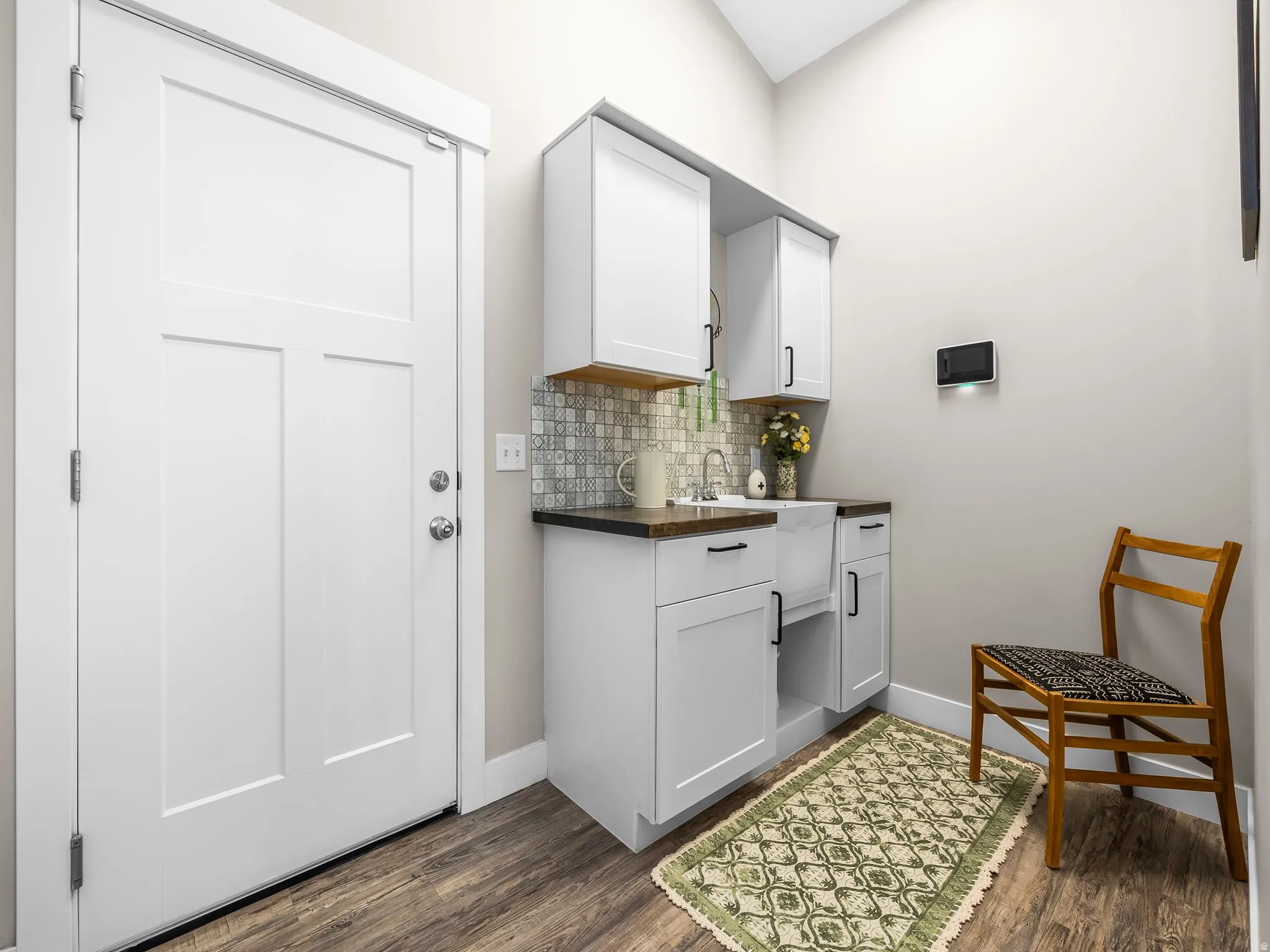 Utility area featuring white shaker-style cabinetry, a white apron-front sink, and dark countertops