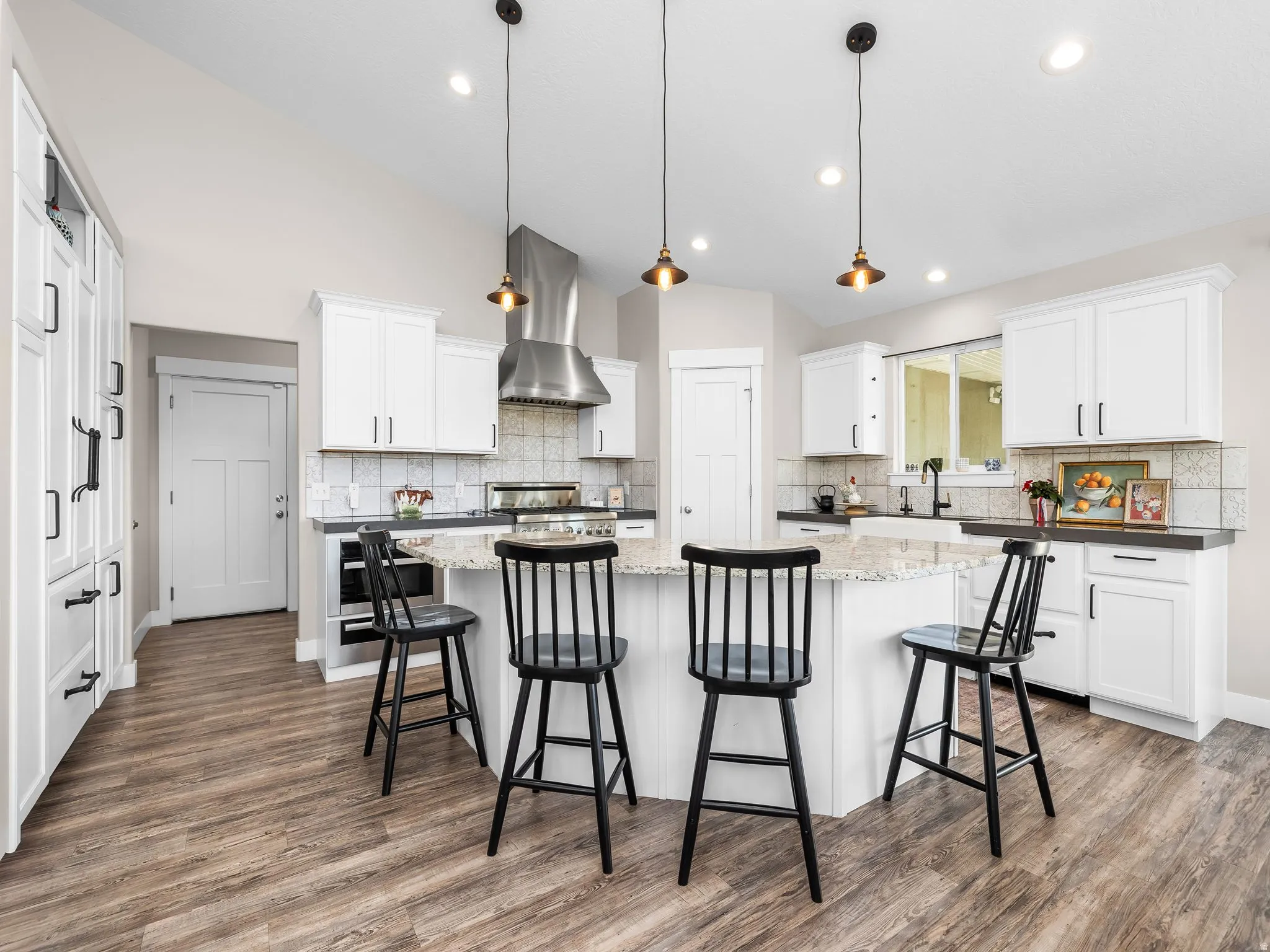 Bright kitchen featuring white cabinetry, a large kitchen island with seating, wood-finish flooring, a stainless steel range hood, and pendant lighting