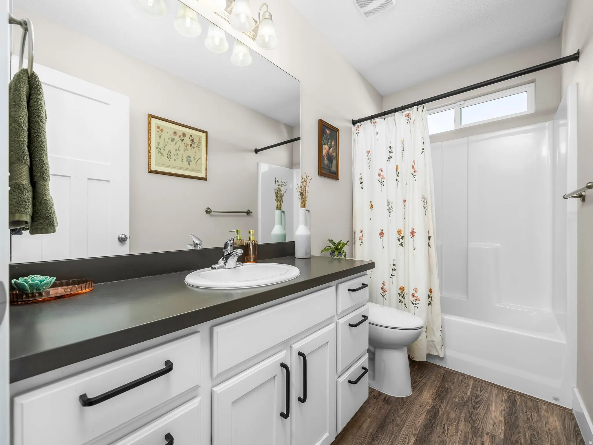 Bathroom featuring a single vanity with a dark countertop, white cabinetry with black hardware, and an undermount sink