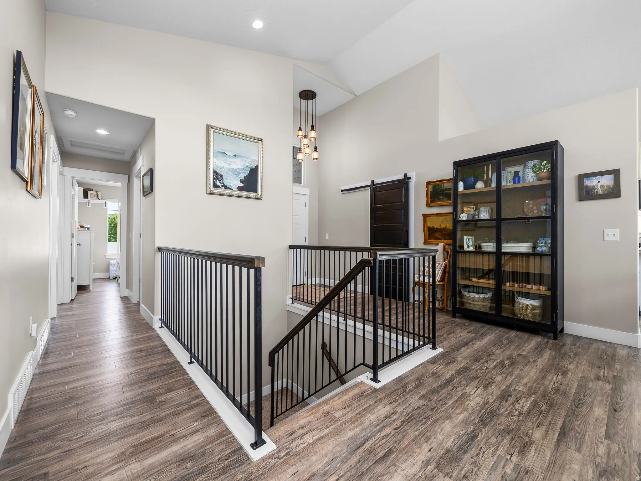 Expansive upper-level landing featuring wood-finish flooring, a modern black iron railing, and vaulted ceilings