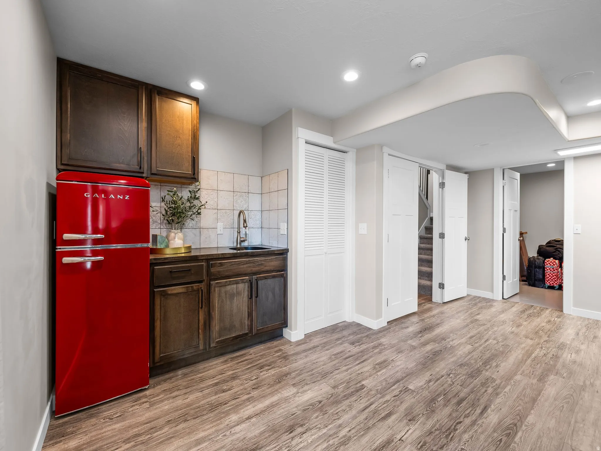 Wet bar area featuring a retro-style red refrigerator, wood cabinetry, stone-look countertop, and a tiled backsplash