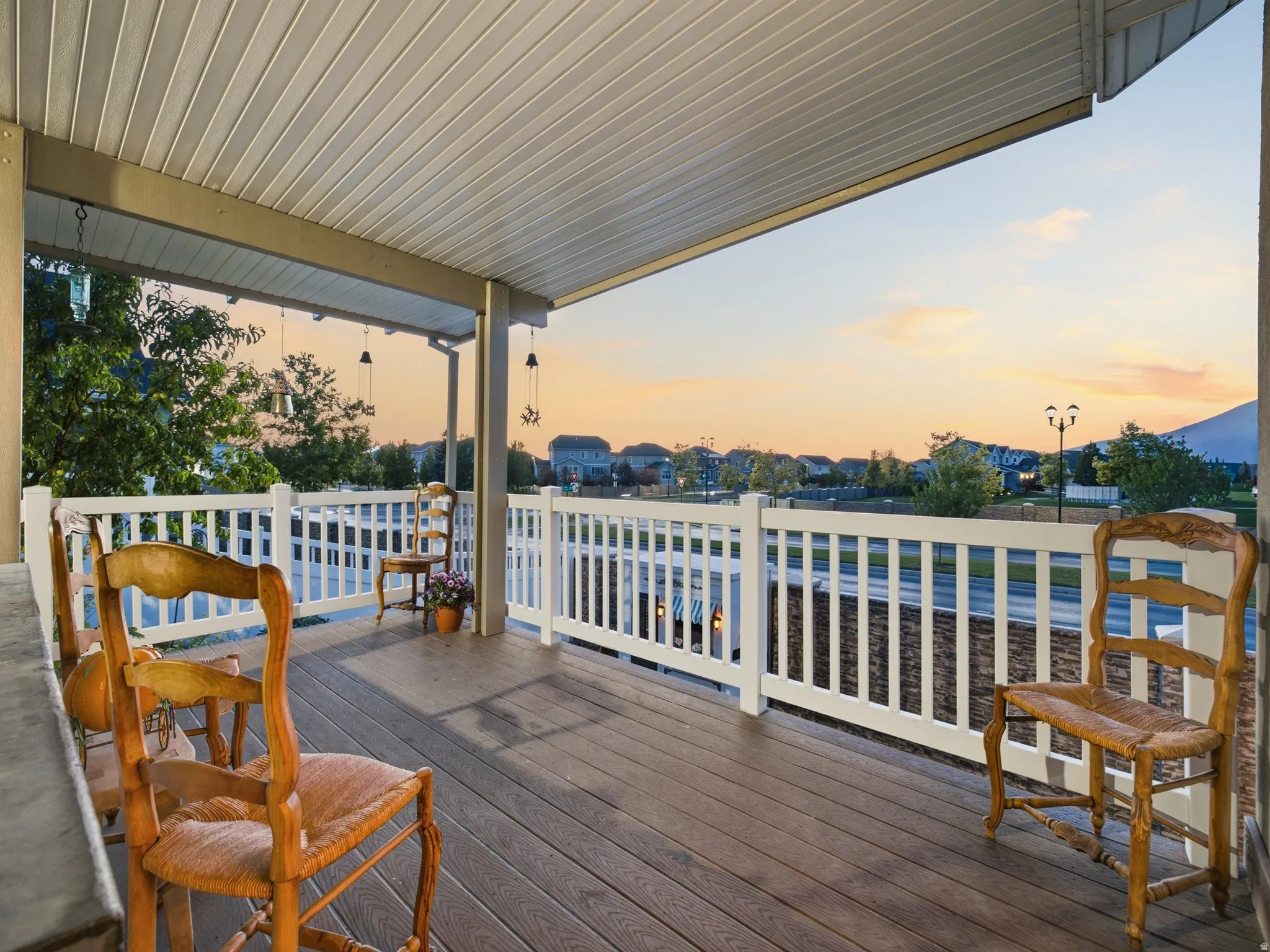 Covered porch featuring wood-finish decking, white railings, and a slatted ceiling with hanging fixtures