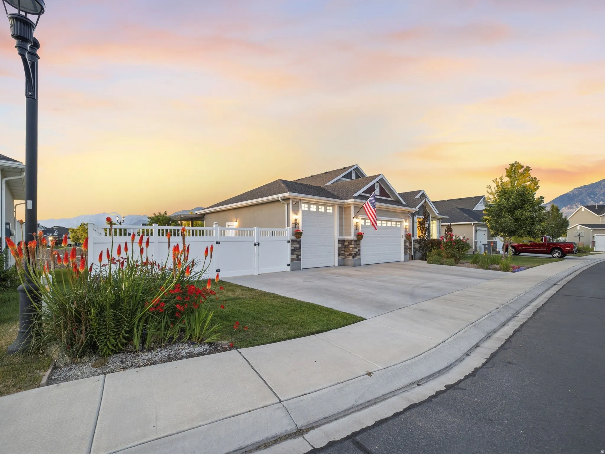 Single-story residence featuring a two-car garage with overhead doors, stacked stone accents on the facade, and a white privacy fence