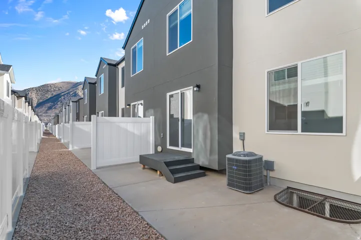 Rear exterior featuring a concrete patio, dark grey deck with steps, and a sliding glass door