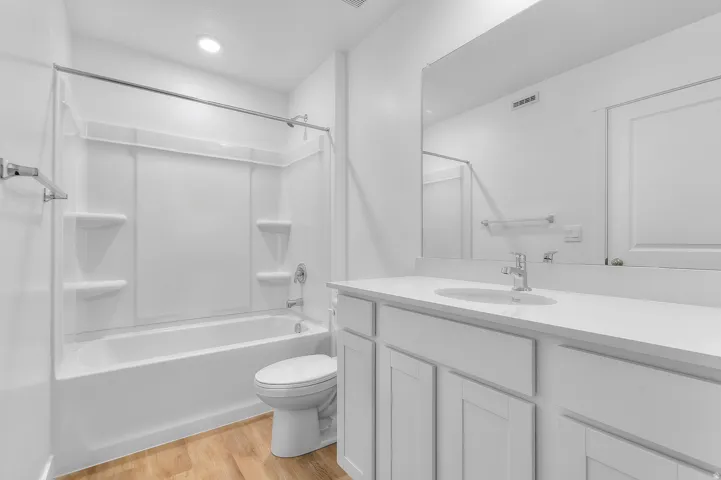 Bathroom with wood-finish flooring, white vanity with integrated sink, chrome faucet, and white countertop