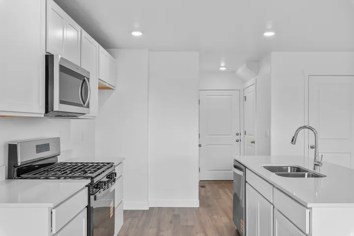 Modern kitchen featuring white cabinetry, stainless steel appliances, light-toned countertops, a gas range, and a kitchen island with an undermount double sink