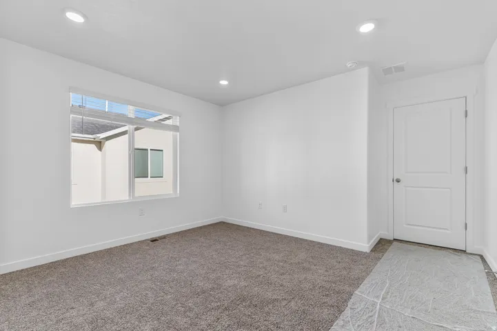 Carpeted interior space featuring white walls, recessed ceiling lighting, and a white two-panel door with a brushed nickel knob