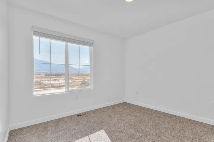 Bright room with large multi-pane window, mountain scenery, light-colored walls, recessed ceiling lighting, and neutral tone carpet flooring