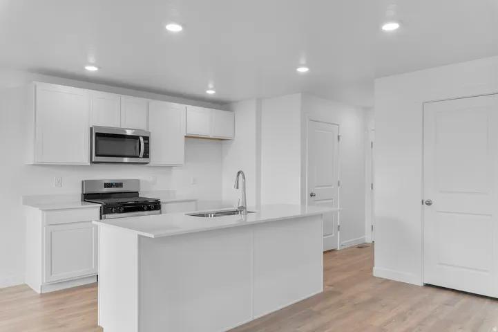 Modern kitchen featuring white shaker-style cabinetry, stainless steel appliances, a center island with sink, light-toned countertops, and wood-finish flooring