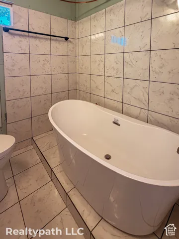 Freestanding oval soaking tub with floor-to-ceiling tile surround and coordinating tile flooring