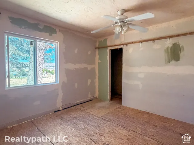 Room featuring a white-framed window, textured ceiling, a ceiling fan with light fixture, and wood-finish subflooring