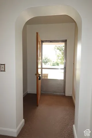 Entryway featuring an arched doorway, wood-panel door with brass hardware, and textured brown carpeting