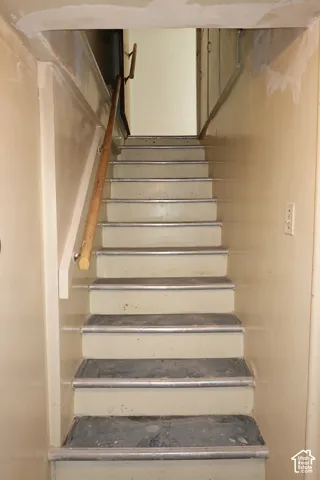 Staircase featuring wood handrail, light-toned walls, and metal stair nosing