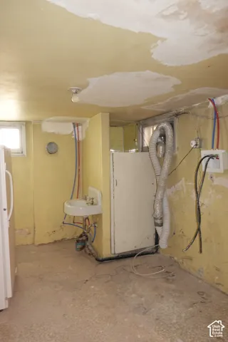 Concrete flooring with a utility sink, exposed piping, and a small window