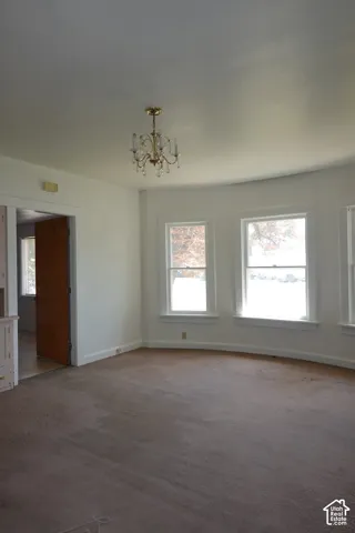 Room featuring a brass chandelier, multiple windows with white trim, and light brown carpeting