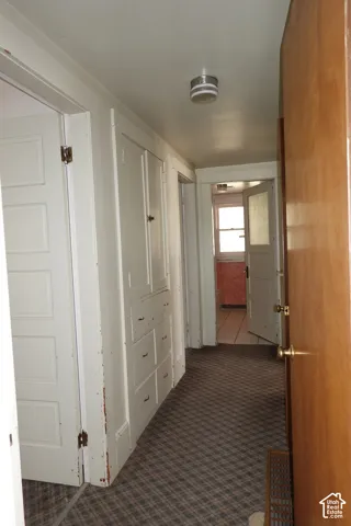 Hallway featuring built-in cabinetry with paneled doors and drawers, a patterned carpet floor, and a white ceiling with a flush-mount light fixture