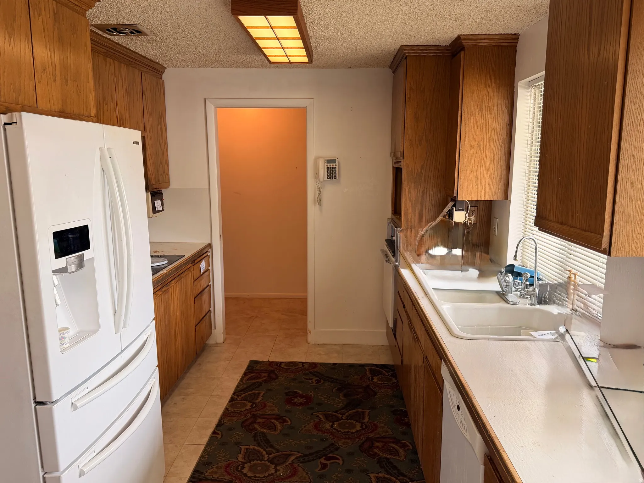 Galley kitchen featuring wood cabinetry, white countertops, a double basin sink, and tile flooring
