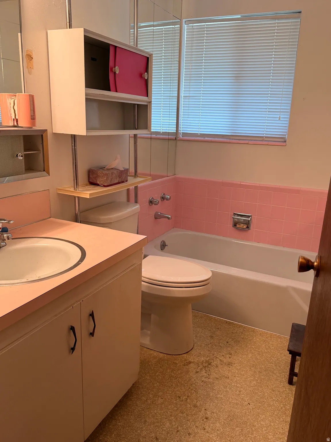 Bathroom featuring a built-in vanity with an integrated sink, a tiled bathtub surround, and a window with horizontal blinds